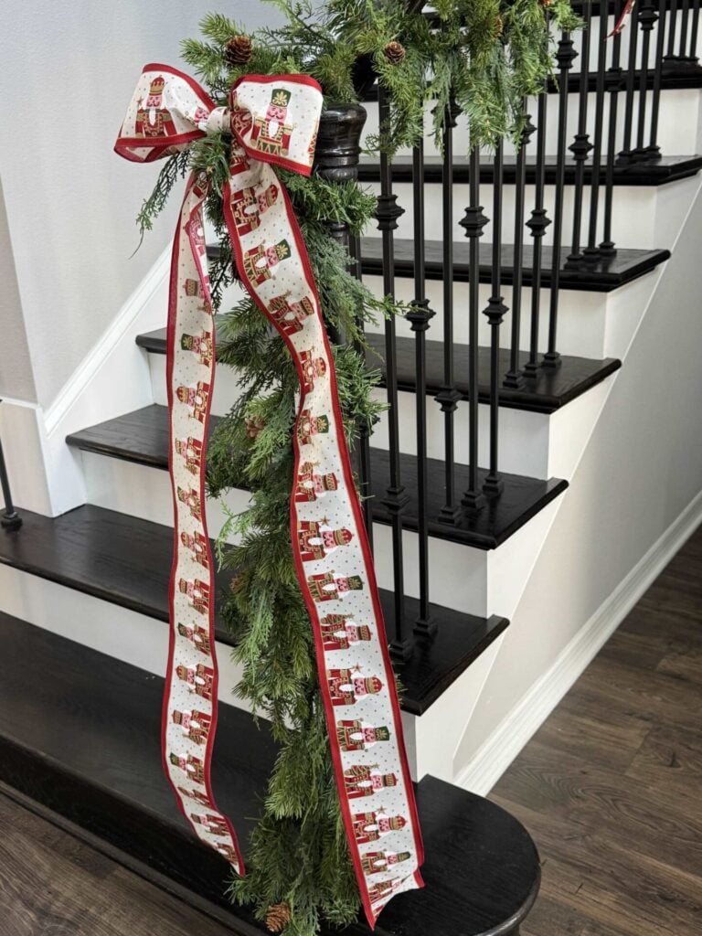 A long bow made from nutcracker ribbon that's attached to an evergreen garland on the end of the stairs. 