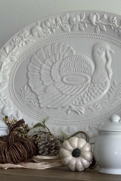 A white turkey platter with a grapevine, a white pumpkin pick, and a white lidded jar. pumpkin