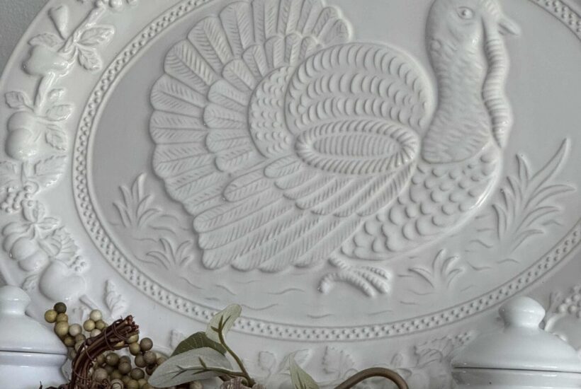 A white turkey platter with a grapevine, a white pumpkin pick, and a white lidded jar. pumpkin