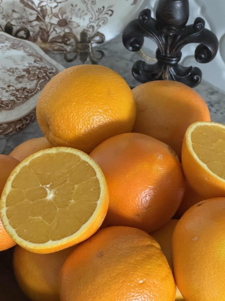 A bowl of oranges with one sliced in half and laying on top.