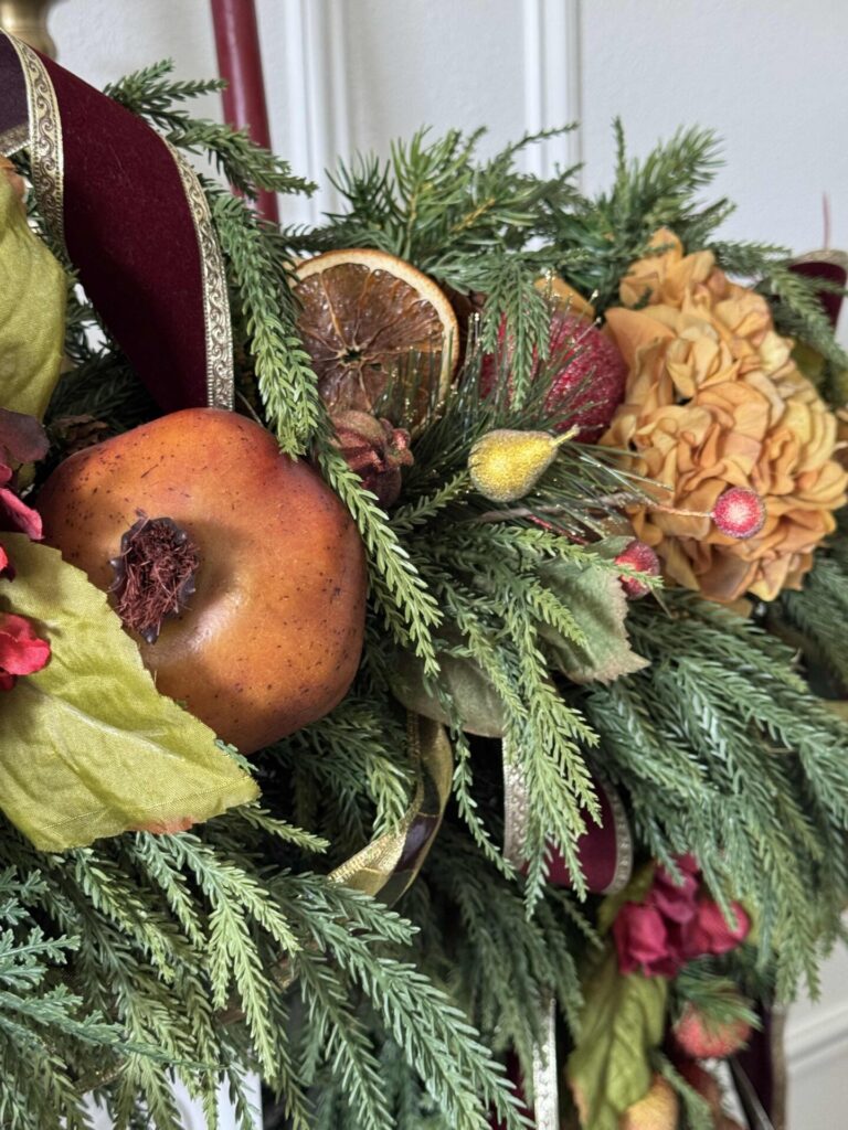 An evergreen garland decorated with faux flowers, fruit, and dried orange slices. 