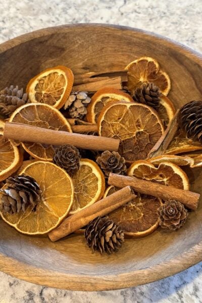 Dried orange slices, pinecones, and cinnamon sticks in a wooden bowl.