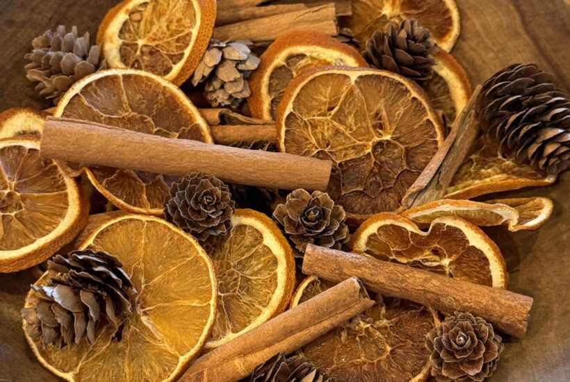 Dried orange slices, pinecones, and cinnamon sticks in a wooden bowl.