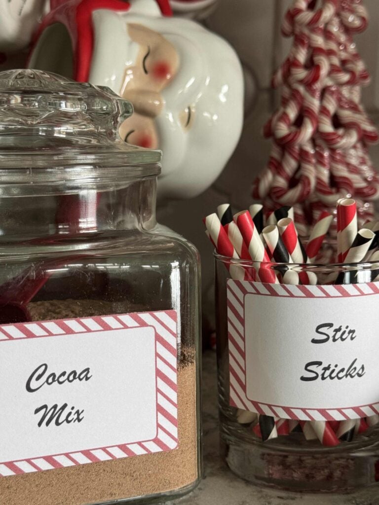 Cocoa mix in a glass jar next to a glass holding stir sticks. 