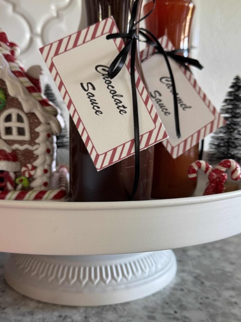 Two bottles of caramel and chocolate sauce with peppermint labels tied to them. 