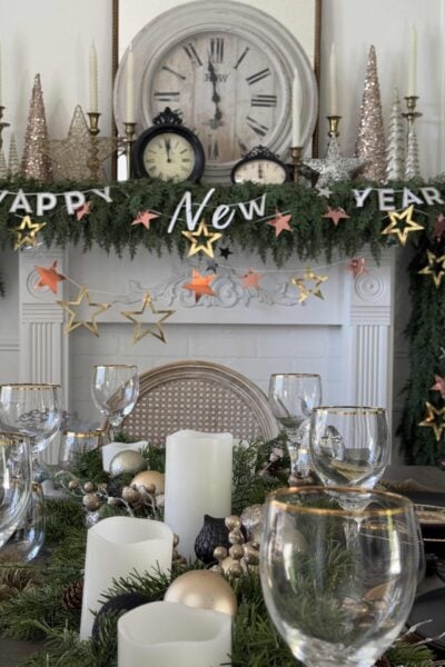 A table and mantel decorated with greenery and a New Year's Eve garland.