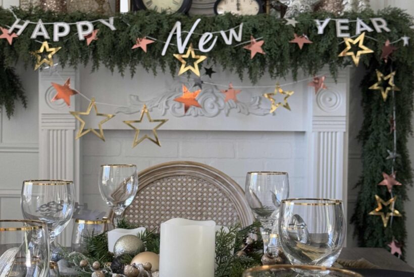 A table and mantel decorated with greenery and a New Year's Eve garland.