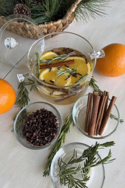 Winter simmer pot surrounded by oranges and bowls of cloves, cinnamon sticks, and rosemary.