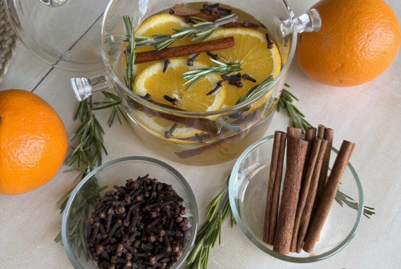 Winter simmer pot surrounded by oranges and bowls of cloves, cinnamon sticks, and rosemary.
