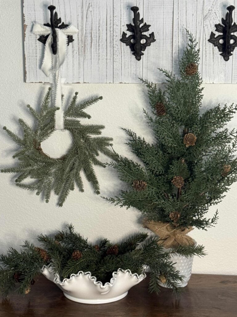 Vignette with tabletop tree in a milk glass bowl, evergreen picks in a bowl and a mini wreath hanging on a hook. 