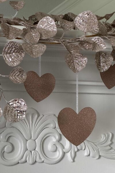 DIY Glitter Hearts hanging on a mantel with a glittered eucalyptus garland.