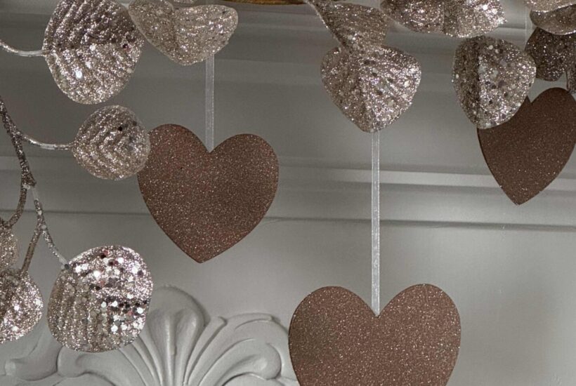 DIY Glitter Hearts hanging on a mantel with a glittered eucalyptus garland.