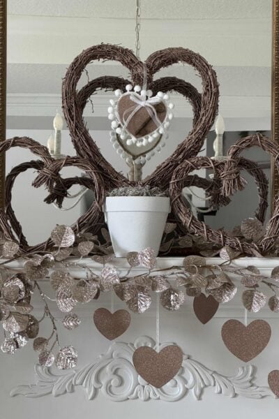 A rose gold grapevine heart in a white pot with a hanging heart inside it.