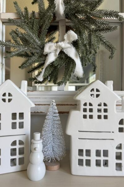 Two white ceramic houses, a snowman, and a white bottle brush tree.