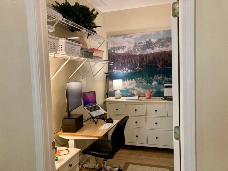 An organized office with a desk, dresser, and wire shelves inside a walk in closet. 