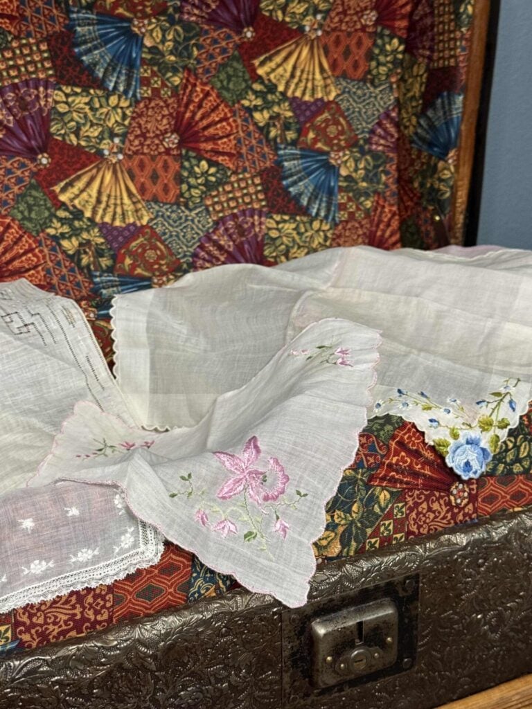 An opened vintage trunk with hankies spread over it. 
