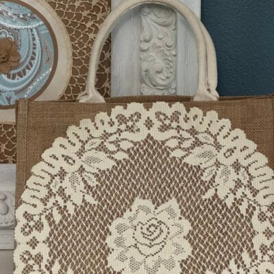 A burlap tote bag with a lace doily attached to the front of it.