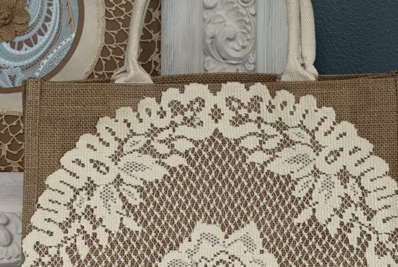 A burlap tote bag with a lace doily attached to the front of it.