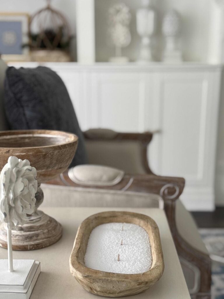 A DIY candle with three wicks in a wooden bowl sitting on a living room table.