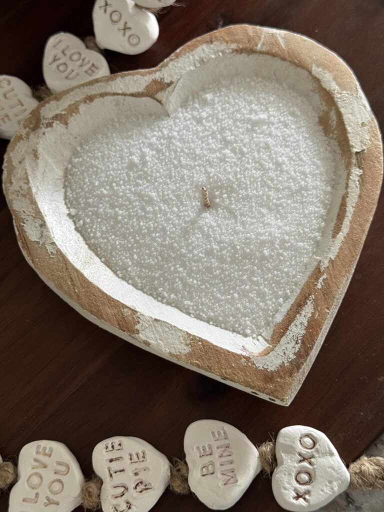 A wood heart bowl filled with white sand candle wax and a wick.