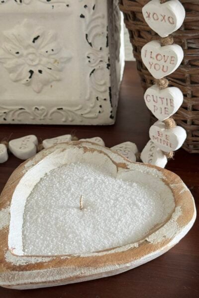 Sand wax candle in a heart-shaped wood bowl next to an air-dry clay conversation heart garland.