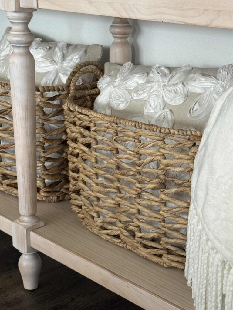Beige and white spring pillows in woven baskets under a console table. 