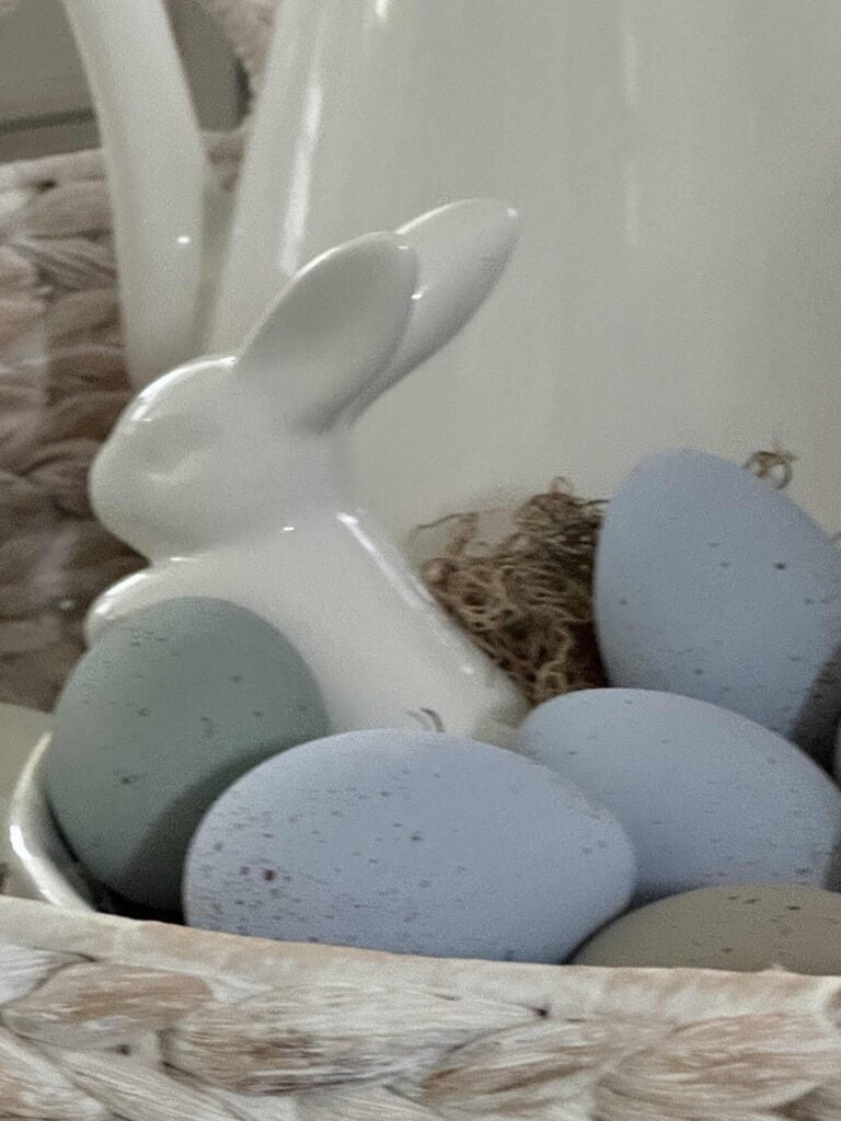  A white ceramic bowl with a bunny leaning over the side and filled with speckled eggs. 