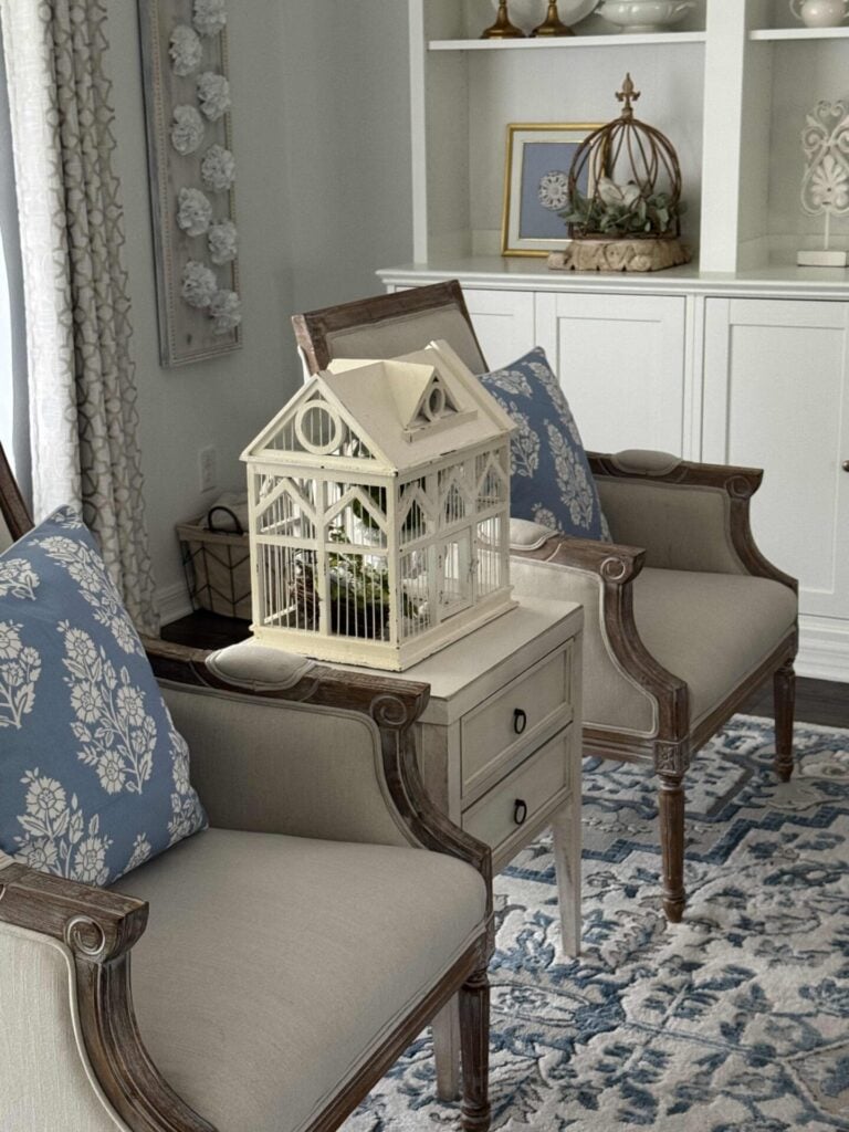Living room chairs with blue and white block print pillows and a table in between holding a white bird cage. 