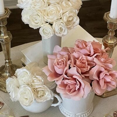A Valentine's table with three vases of roses and a heart garland.
