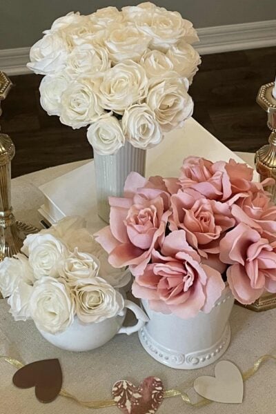A Valentine's table with three vases of roses and a heart garland.