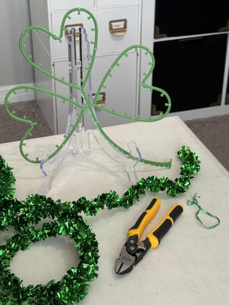 Plastic shamrock form with green tinsel and wire cutters laying beside it. 