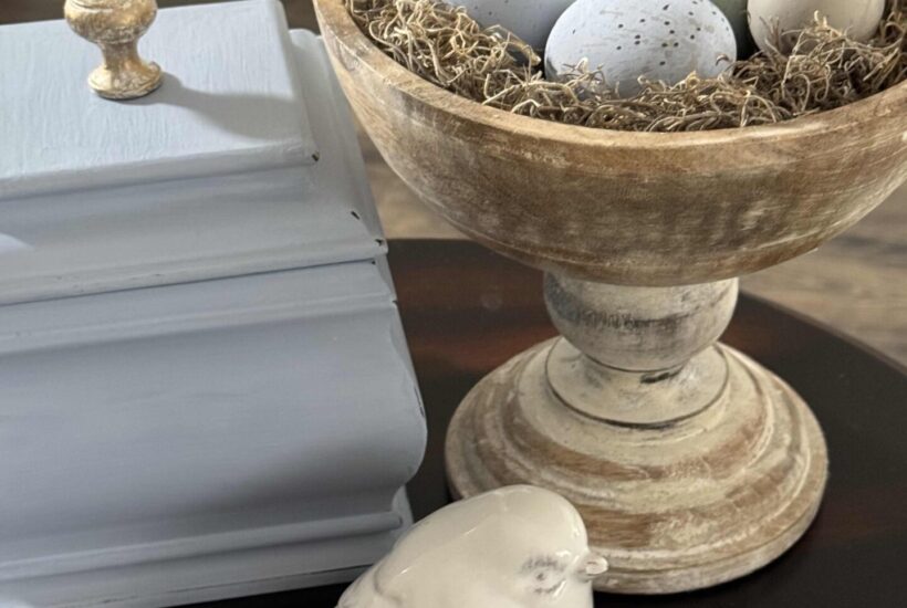DIY speckled Easter eggs in a wood bowl, next to a blue box and a white ceramic bird.