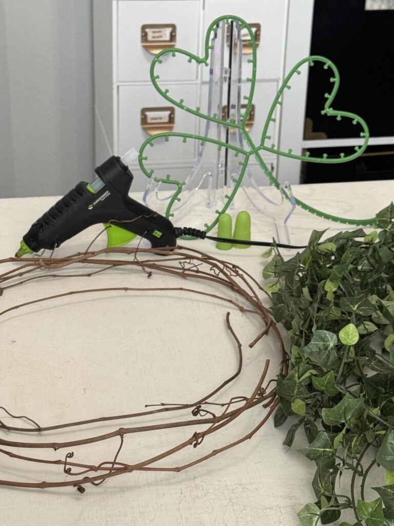 Plastic shamrock form, a glue gun, pieces of grapevine, and an ivy garland. 
