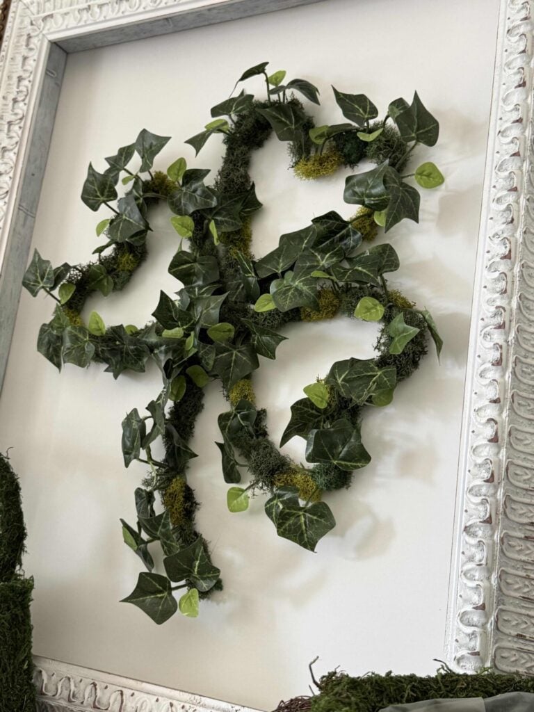 A DIY St. Patrick's shamrock wreath hanging in a white picture frame.
