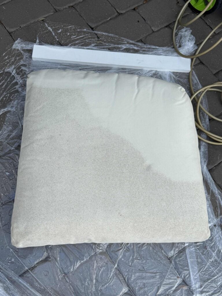 An outdoor cream couch cushion that is half covered in pollen. 