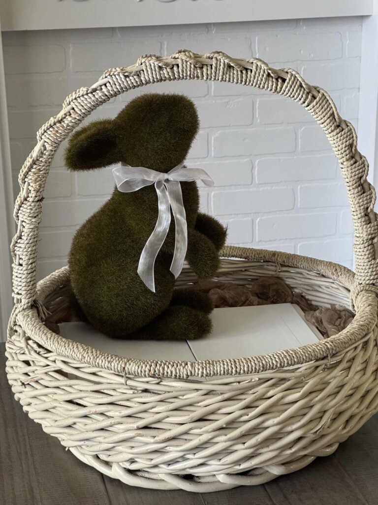 A white vintage basket with a moss bunny inside. 
