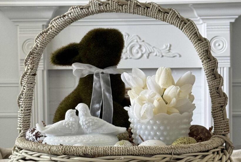 DIY Easter Centerpiece in a white basket with a moss bunny, milk glass bowl with tulips, and a milk glass lovebird trinket dish, surrounded by decoupage eggs.