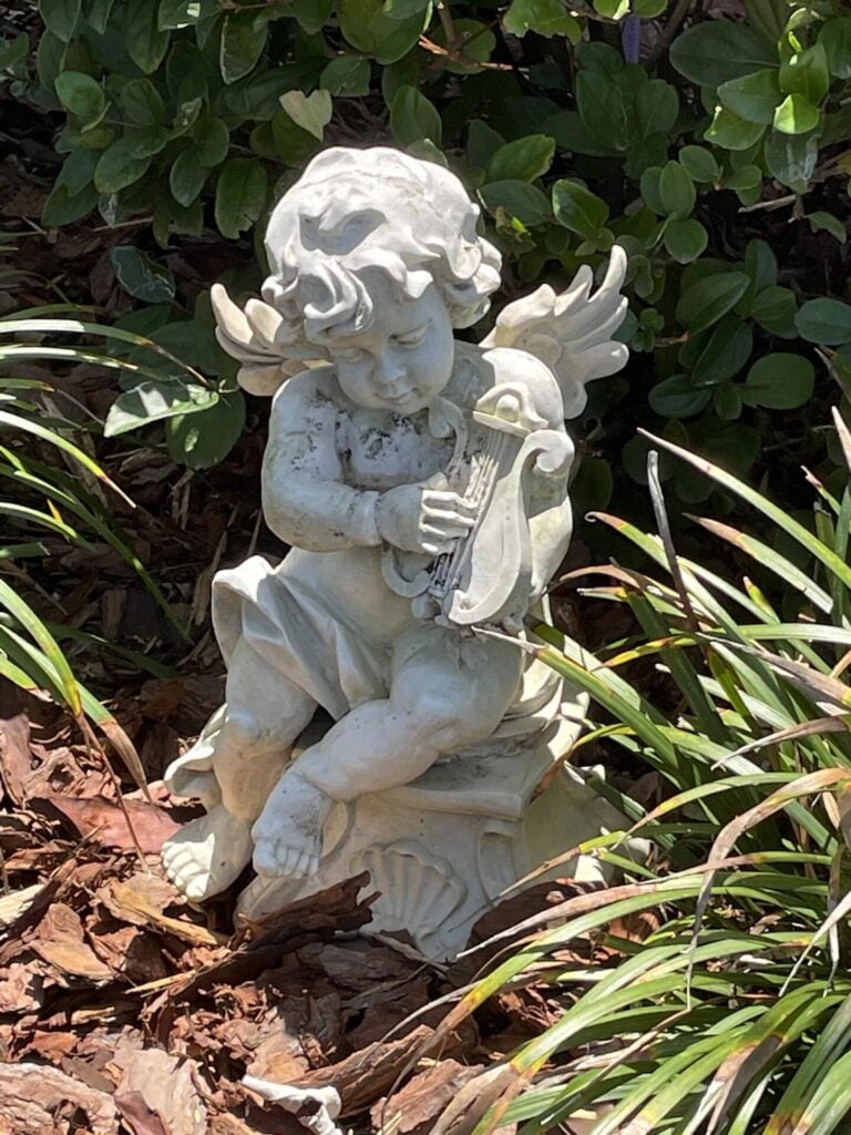 An angel statue in a mulched flower bed. 