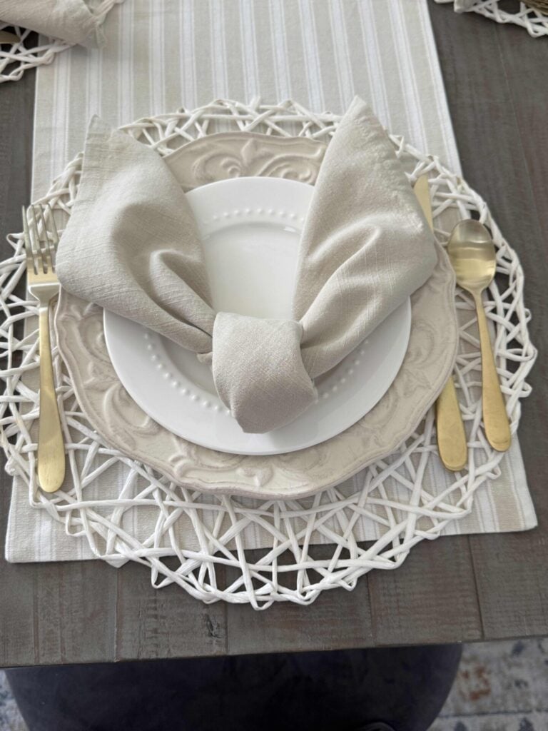 A place setting with white and cream plates with a napkin folded like bunny ears. 