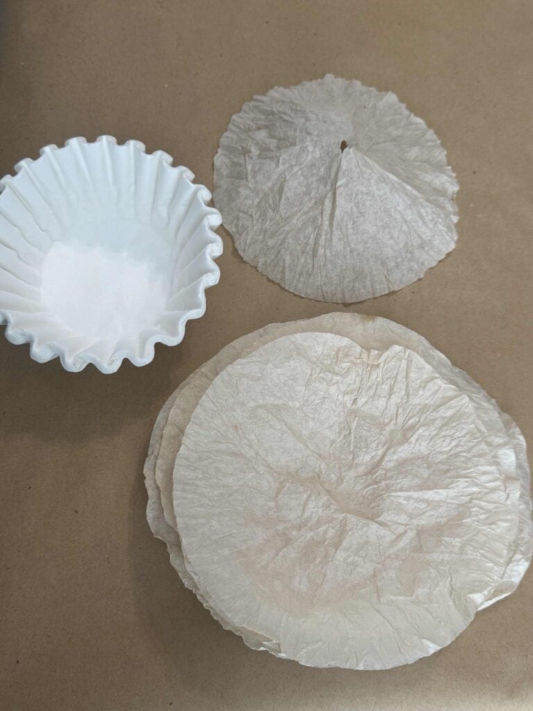 Coffee filters next to other filters that have been soaked in coffee to stain them. One has a hole in the center. 