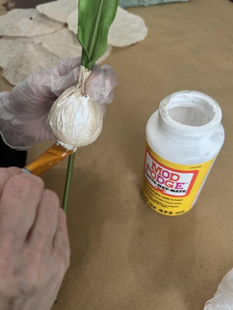 Someone painting Mod Podge on a faux bulb on a tulip. 