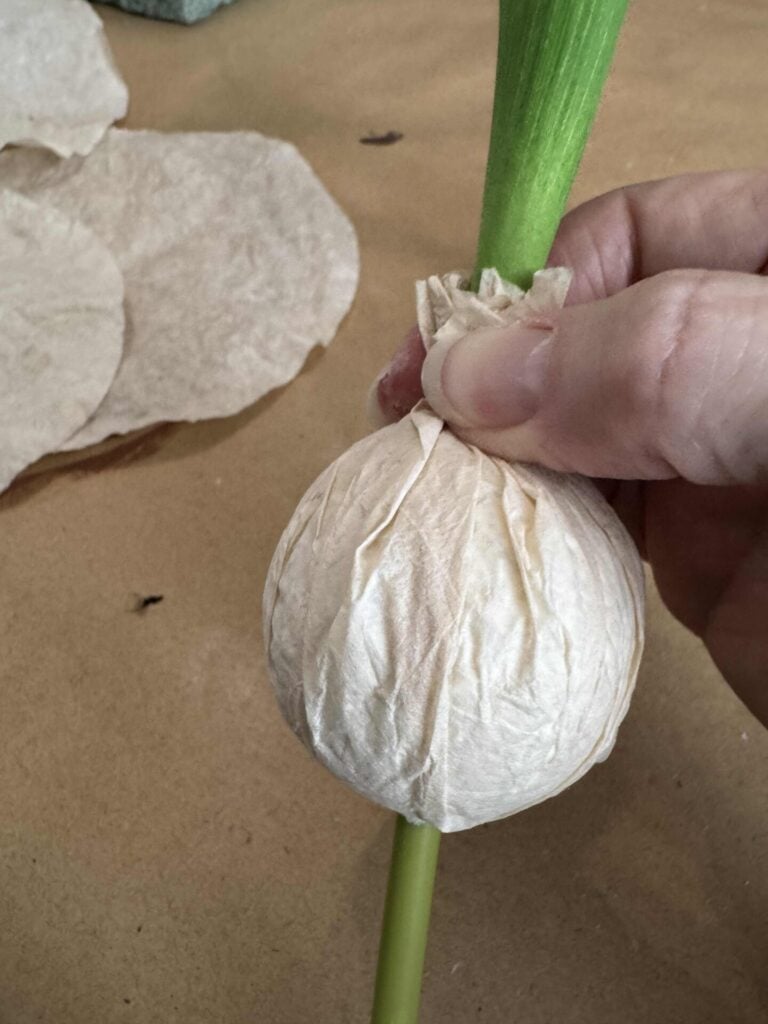 Someone holding a stained coffee filter around a foam ball attached to a tulip stem. 