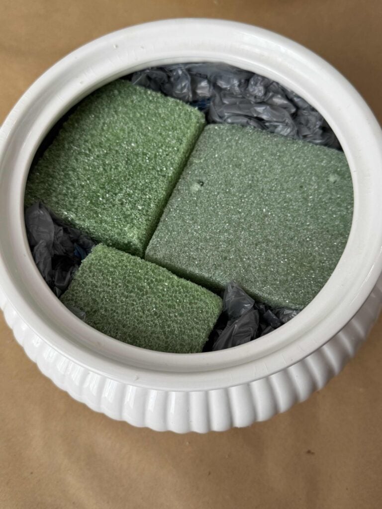 A soup tureen filled with green foam and gray plastic bags. 
