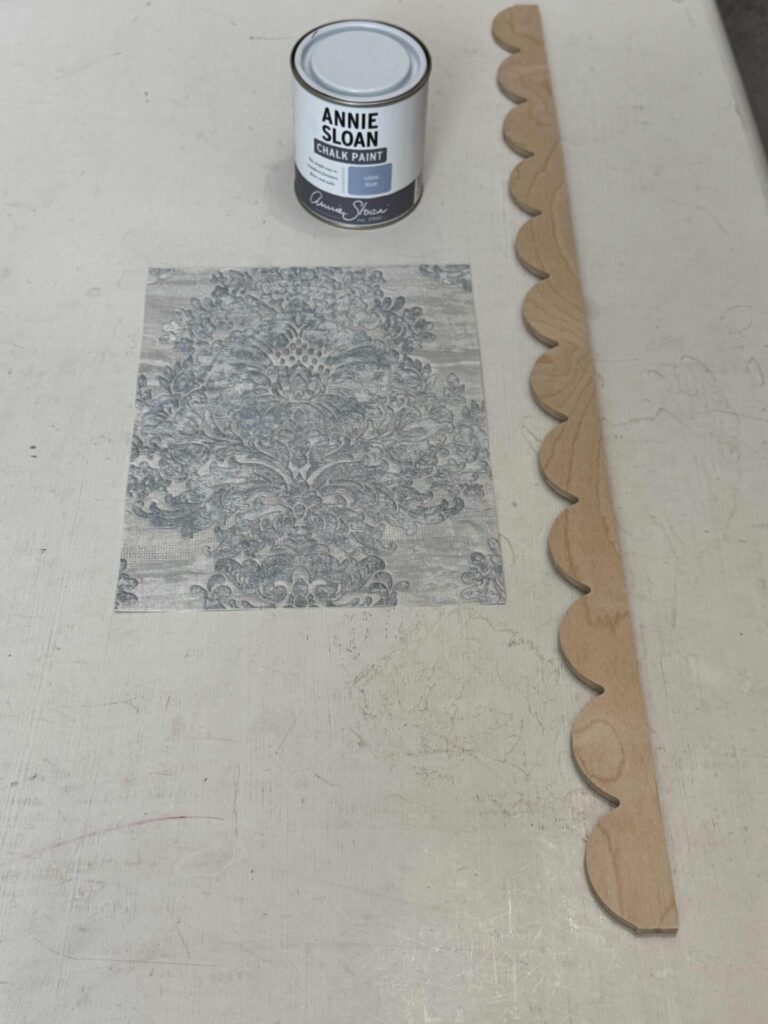 A wallpaper sample, a can of blue paint, and a piece of scalloped wood trim. 