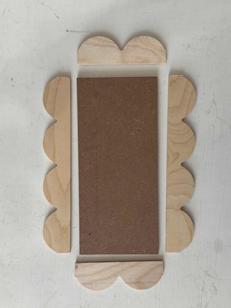 A hardboard rectangle with four pieces of scalloped trim surrounding it. 