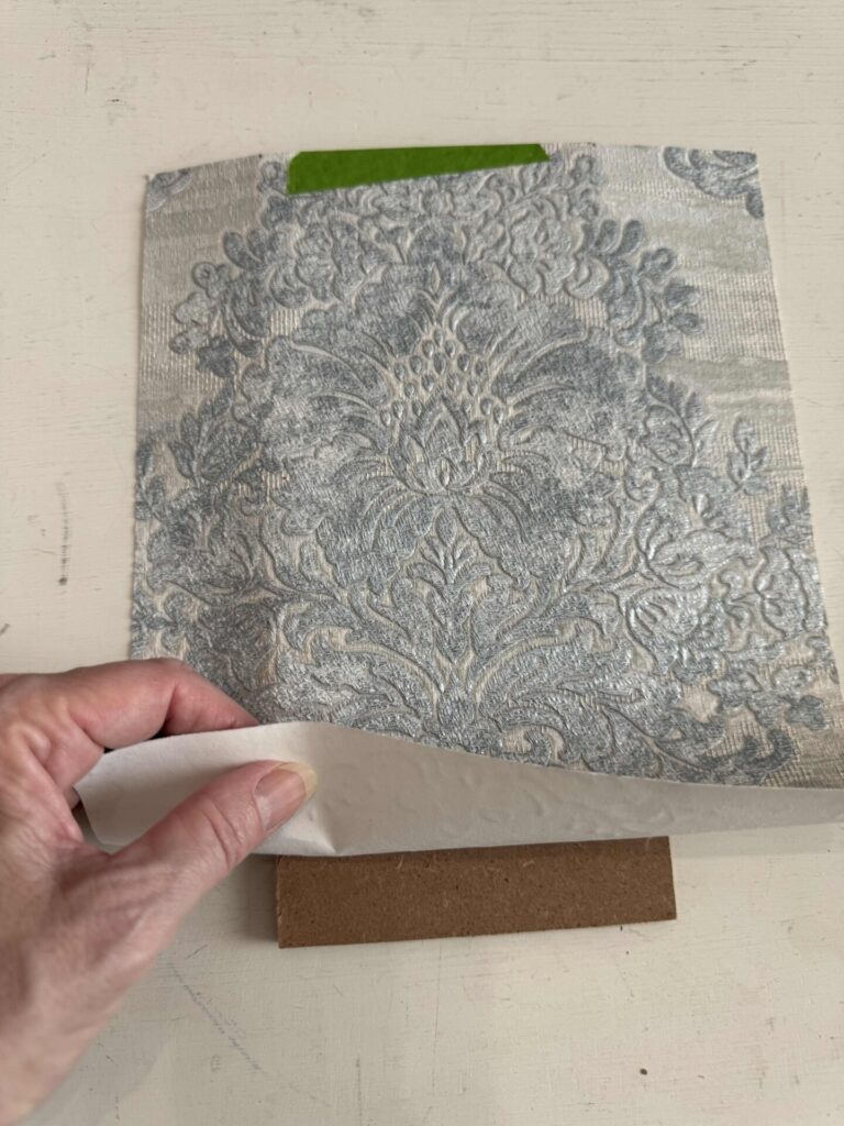 Someone placing a wallpaper sample over a piece of hardboard.