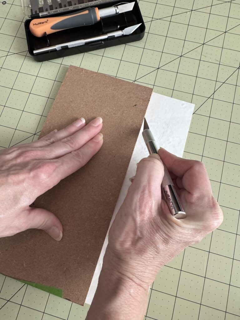 Someone cutting a wallpaper sample with a craft knife and a cutting mat. 