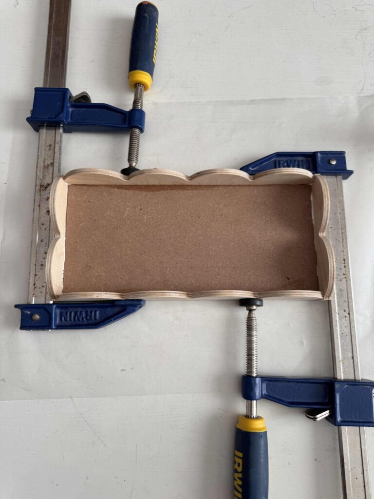 A DIY scalloped wood tray with clamps holding it together while the glue dries. 