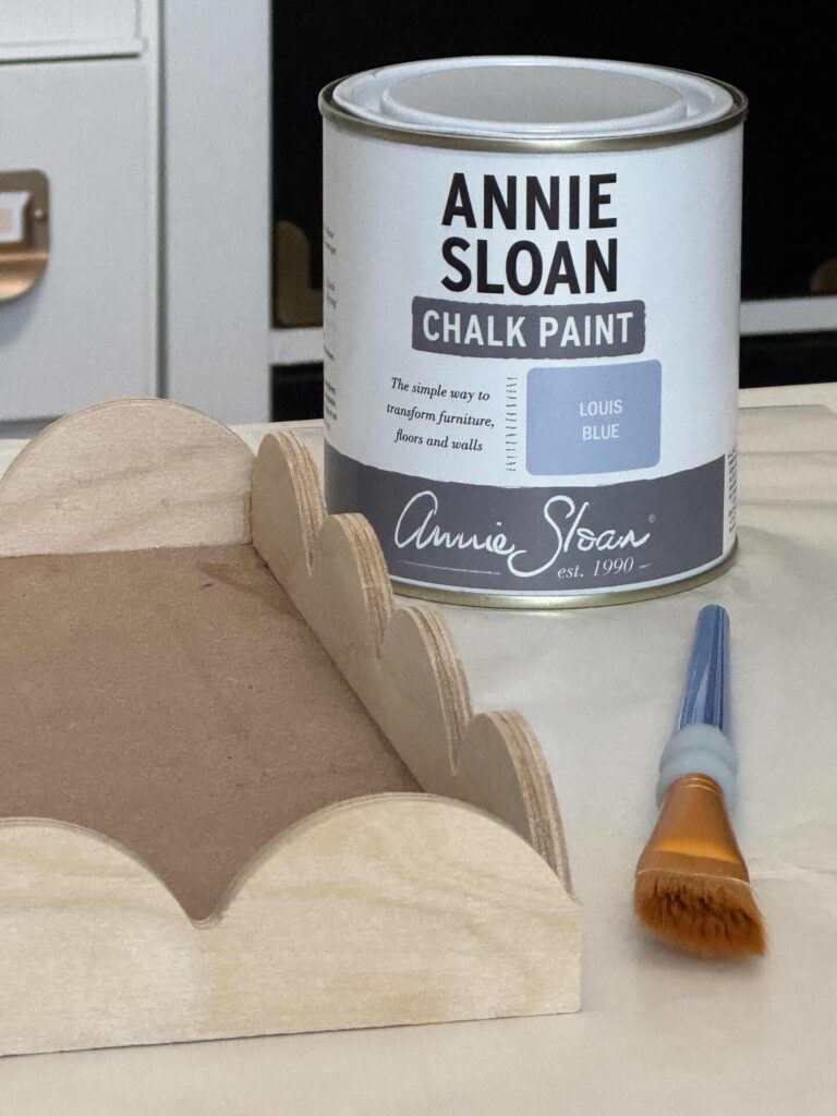 A DIY scalloped wood tray next to a can of blue paint and a paintbrush. 