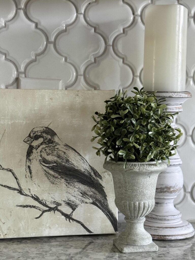 Spring kitchen decor idea #4 is to prop up a spring canvas on a kitchen counter and pair it with a topiary and a white candlestick. 